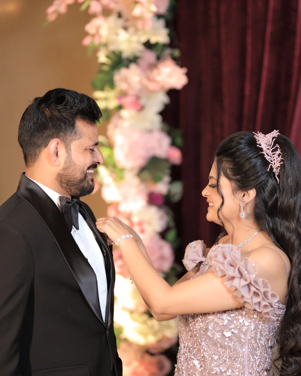 Bride laughing as she straightens the groom’s bow tie