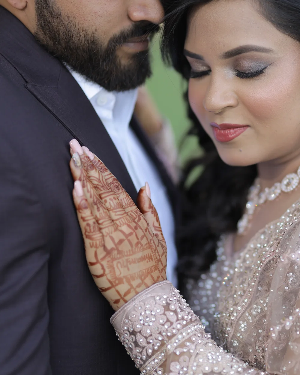 Bride with eyes closed, her hennaed hand resting on the groom’s chest