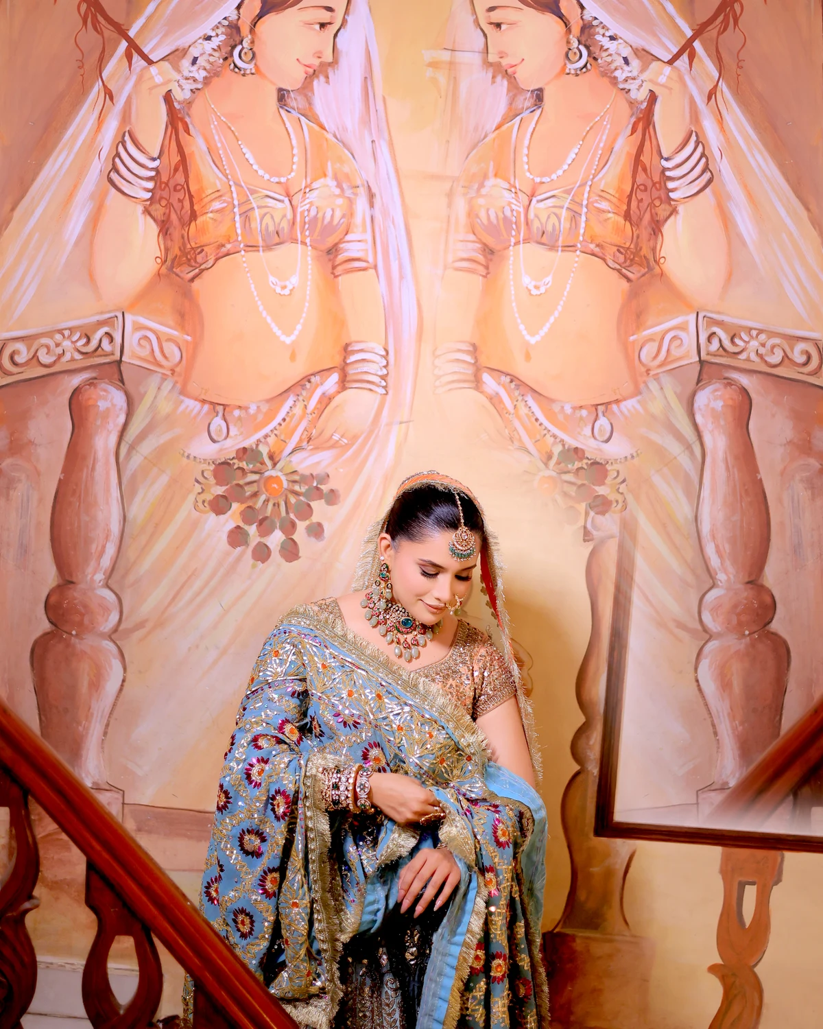 Bride in a blue lehenga seated before a hand-painted mural