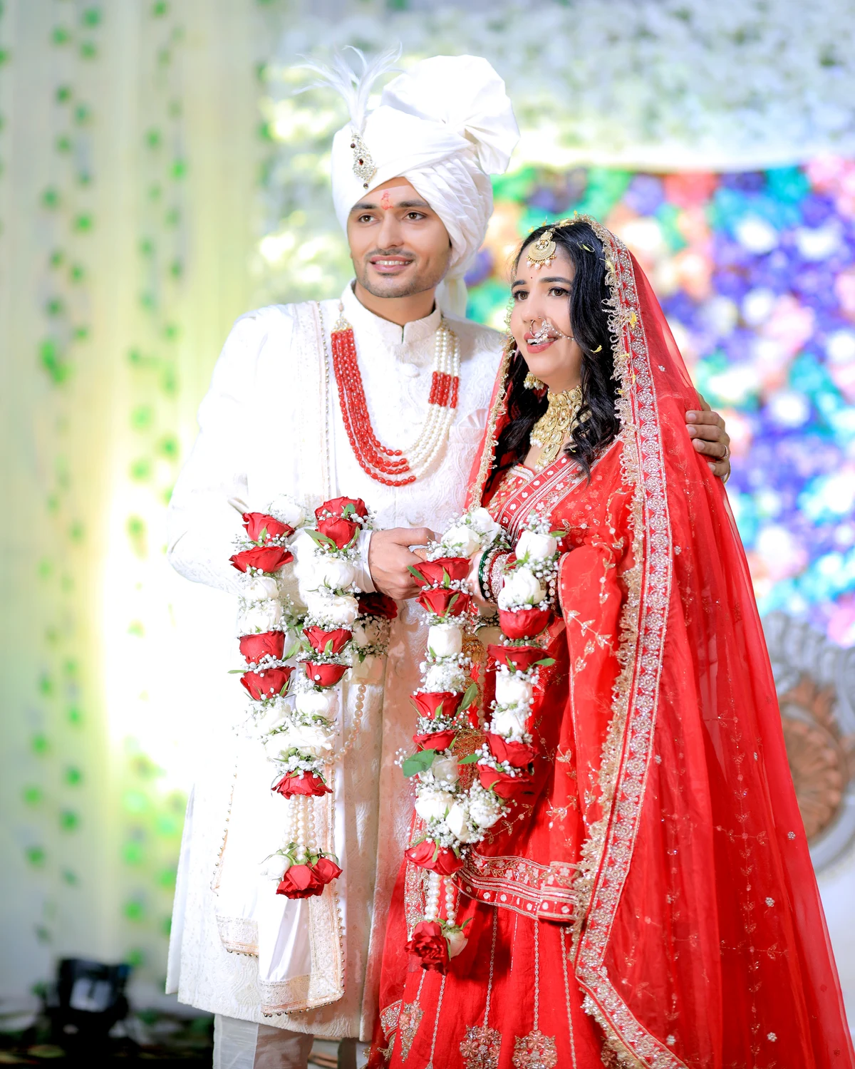 Bride and groom in varmala garlands against colourful lights