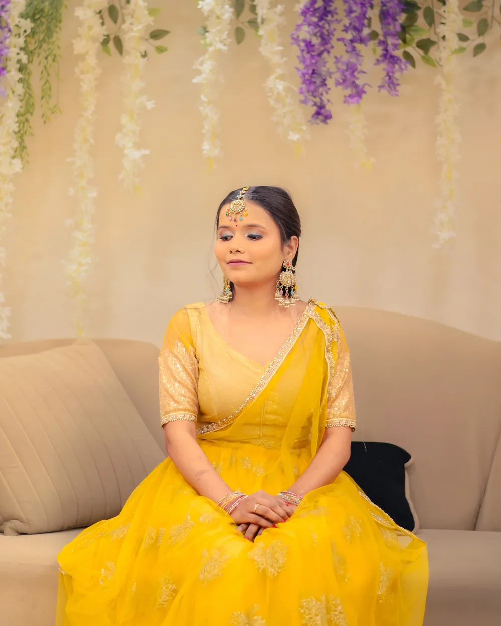 Bride in a yellow lehenga seated beneath hanging flowers