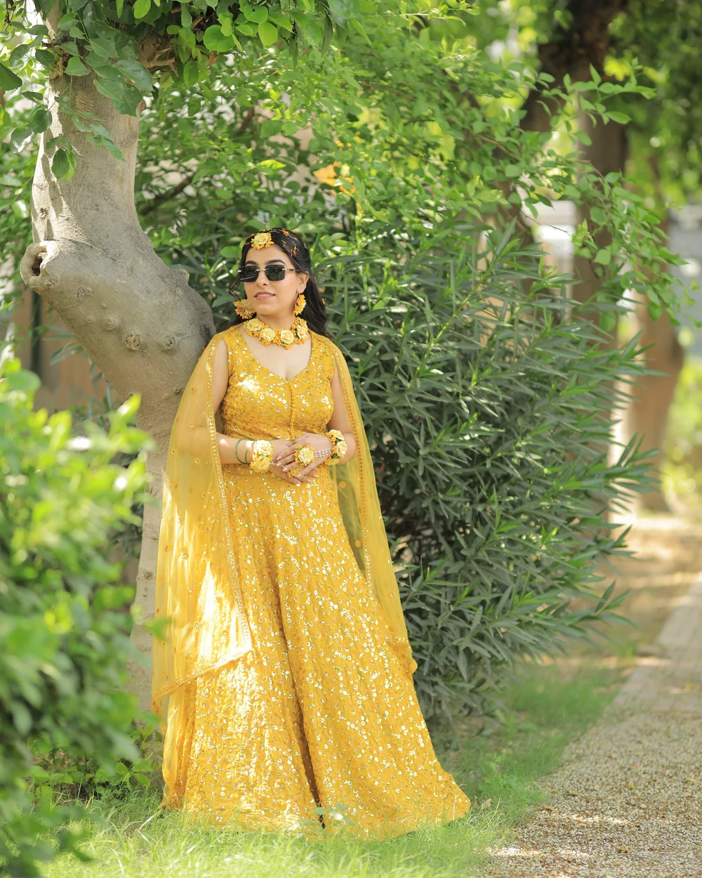 Bride in a yellow lehenga and sunglasses in a garden