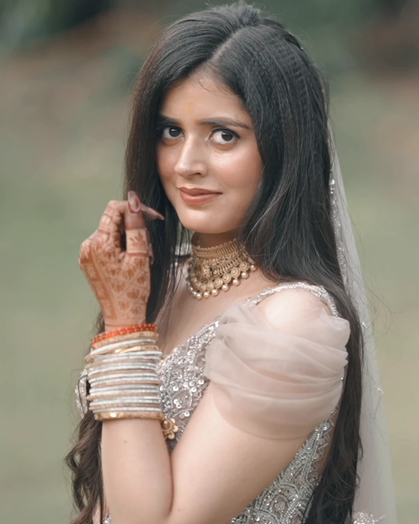 Bride in a blush lehenga smiling with hennaed hands in a garden