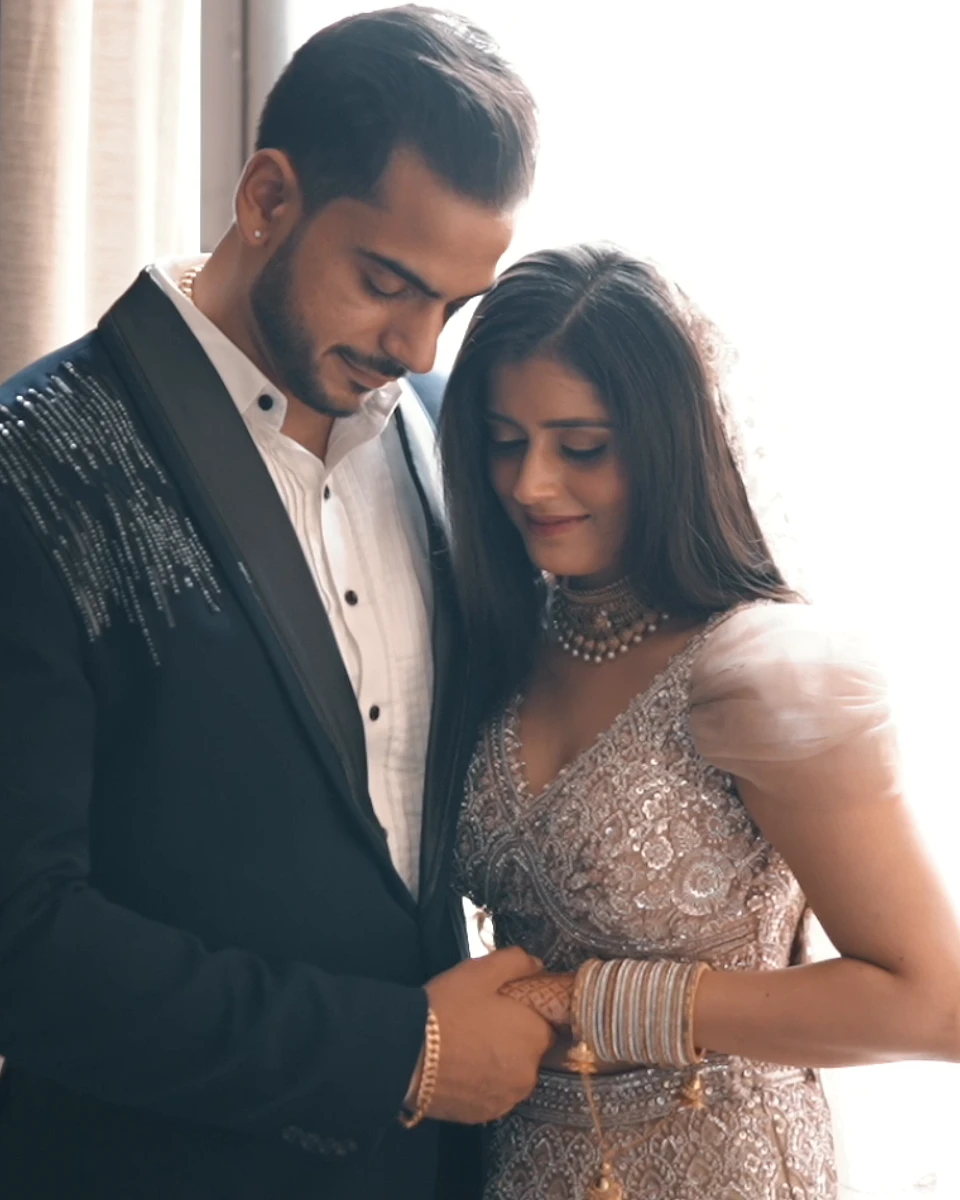 Groom in a black sherwani holding his bride close by a sunlit window