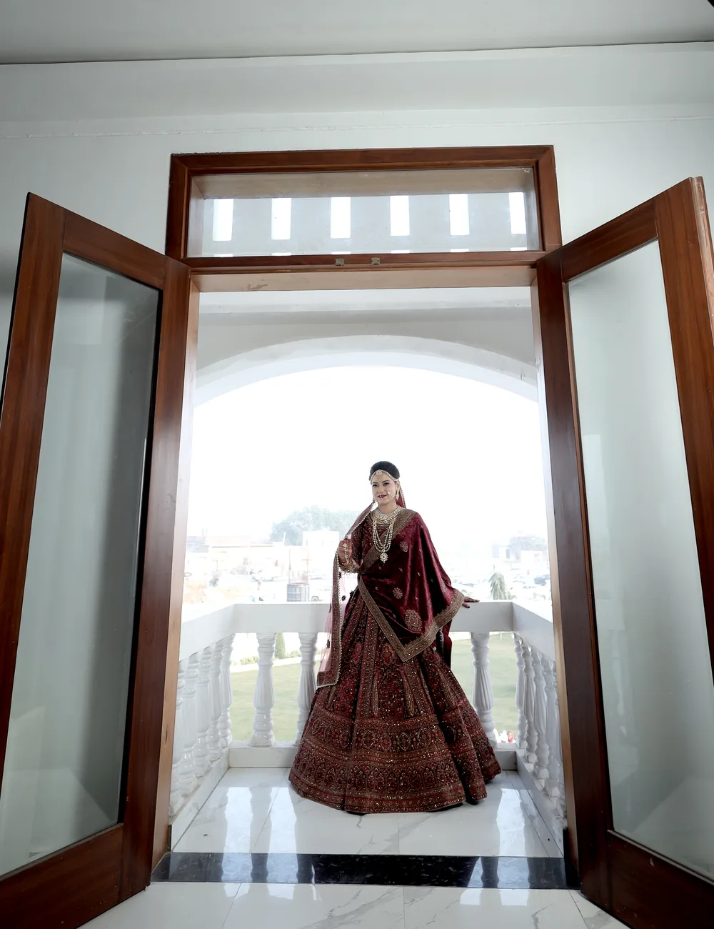 Bride in a maroon lehenga framed by a grand palace doorway