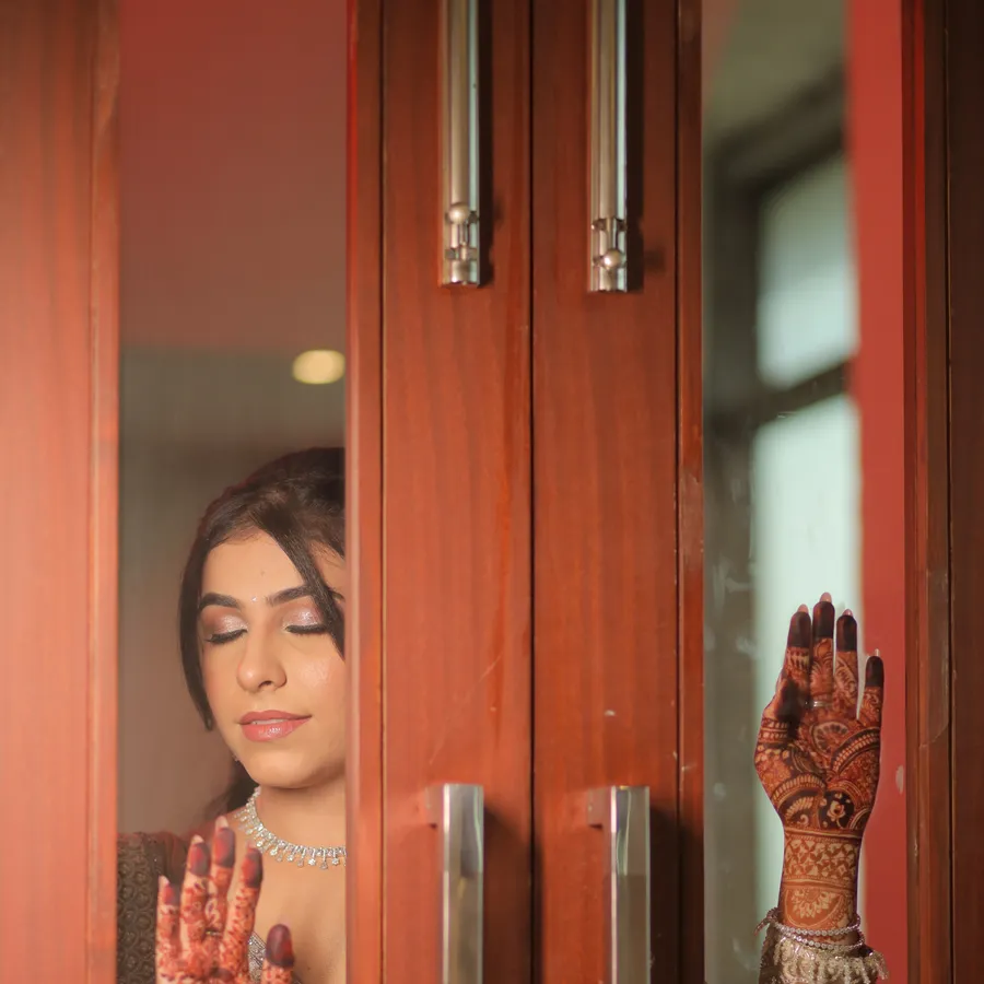 Bride peeking through a wooden door, mehndi on her hand